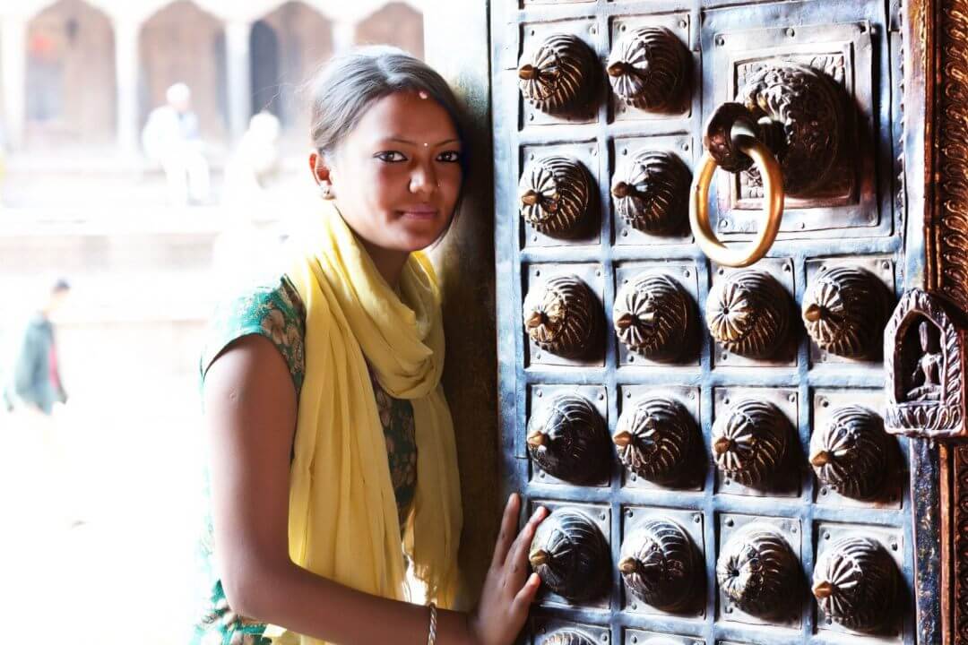 Femme npalaise devant une porte traditionnelle sculpte, symbolisant l’artisanat authentique de Fleur du Npal